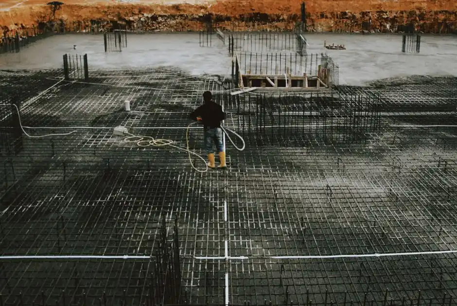 A worker stands on a reinforced concrete foundation, preparing for construction.
